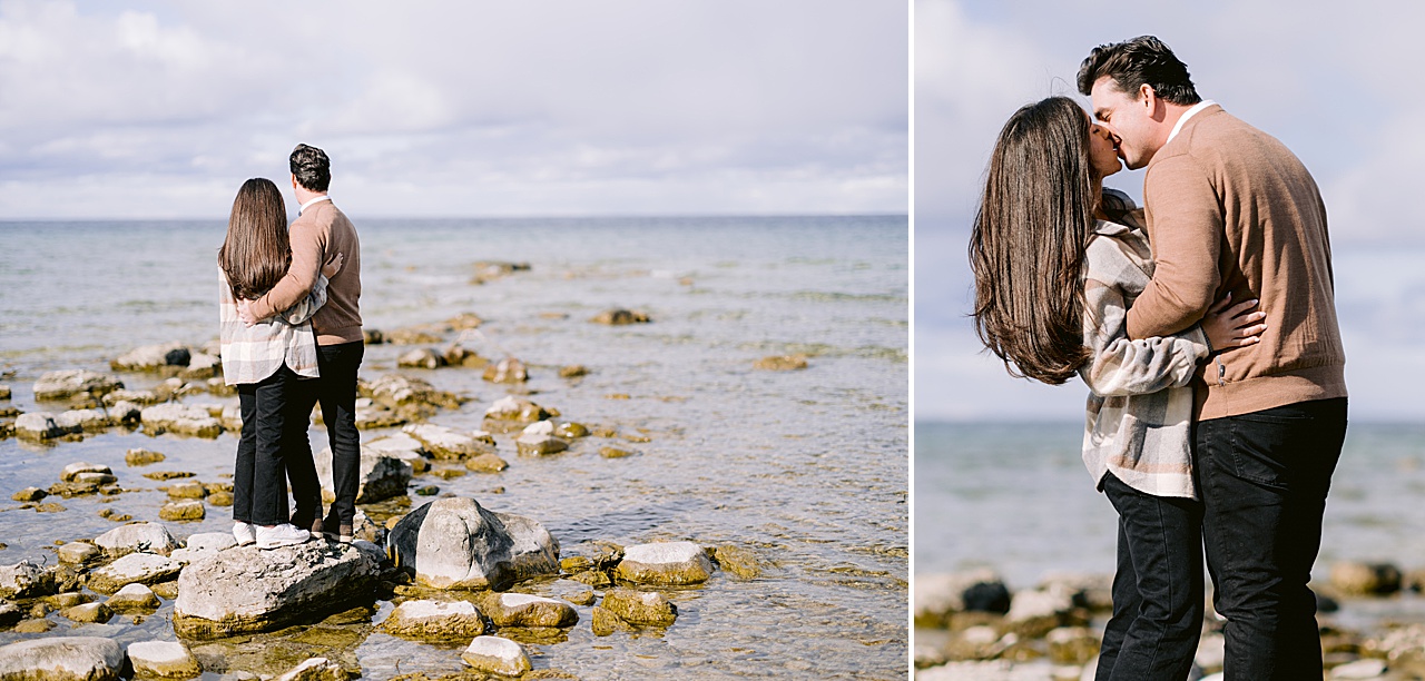 A couple stand on stones in Lake Michigan and kiss for engagement photos