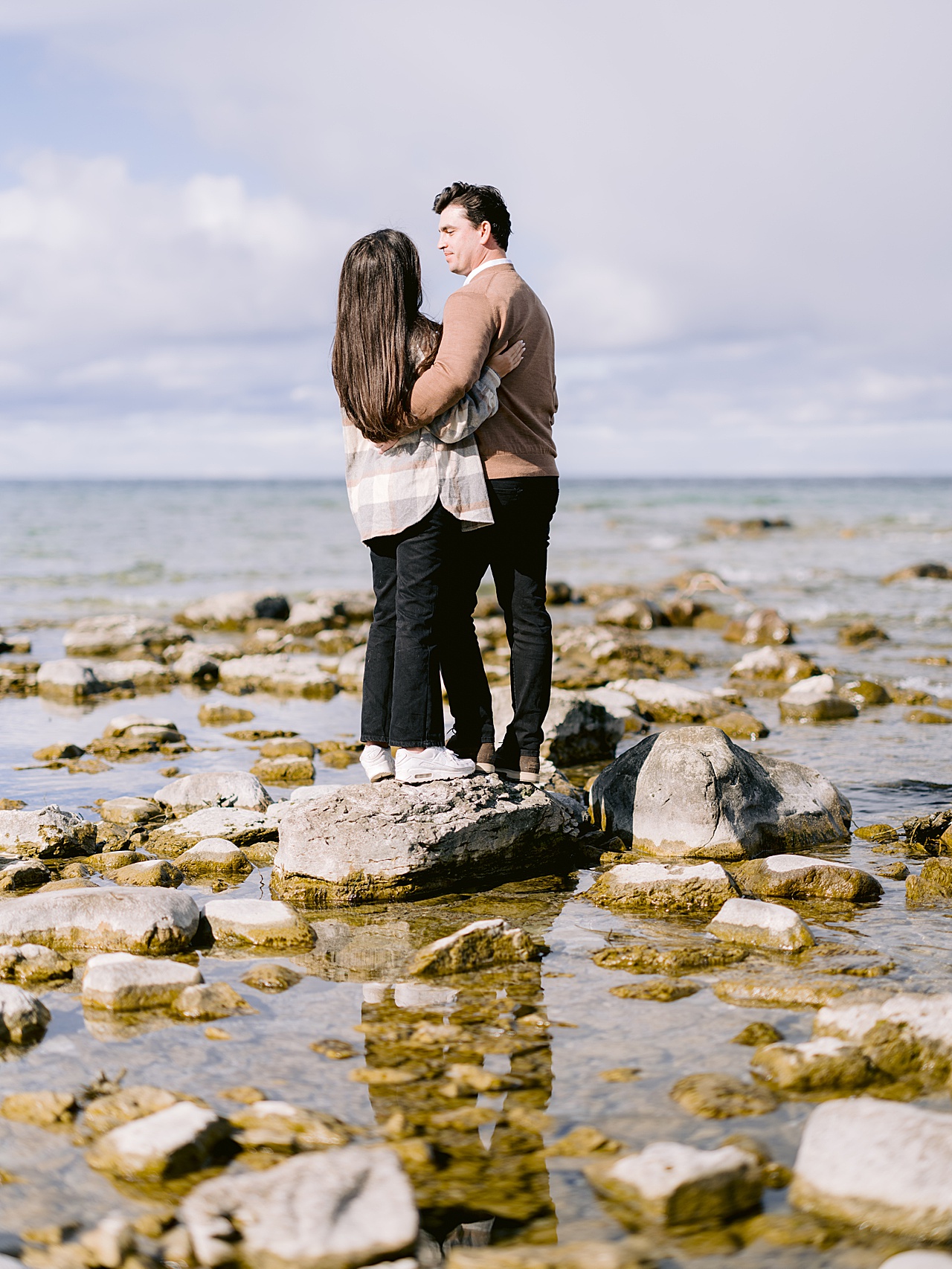 A couple stands on a rock in the water and look at each other in Michigan