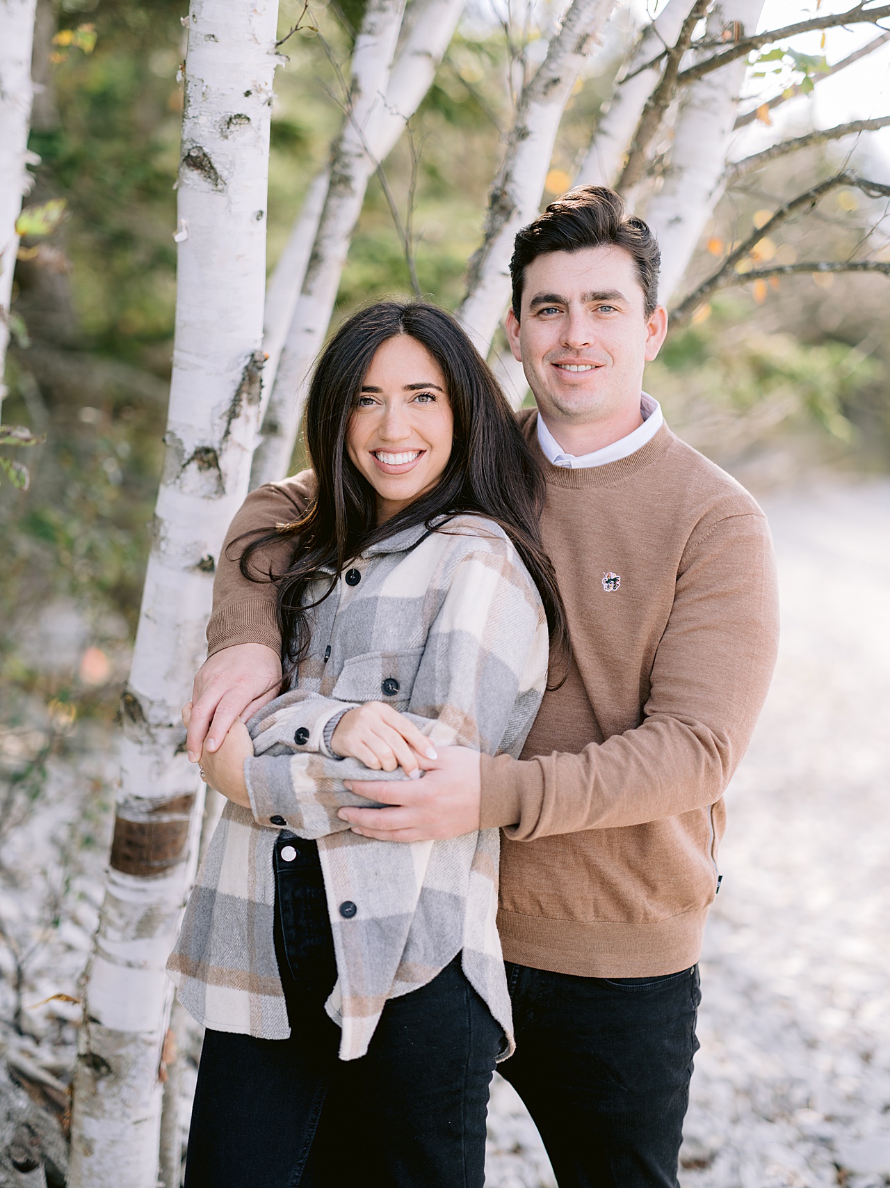 A couple pose for engagement photos next to a birch tree