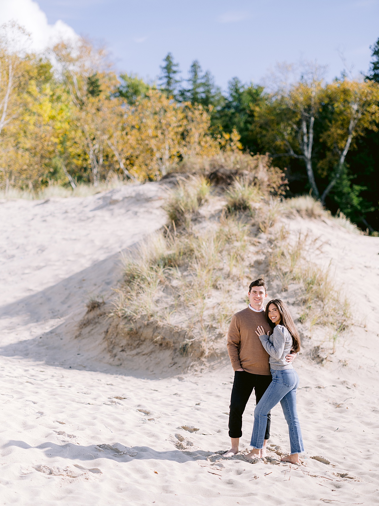 A man and woman smile next to a sandy hill near downtown Petoskey for engagement photography