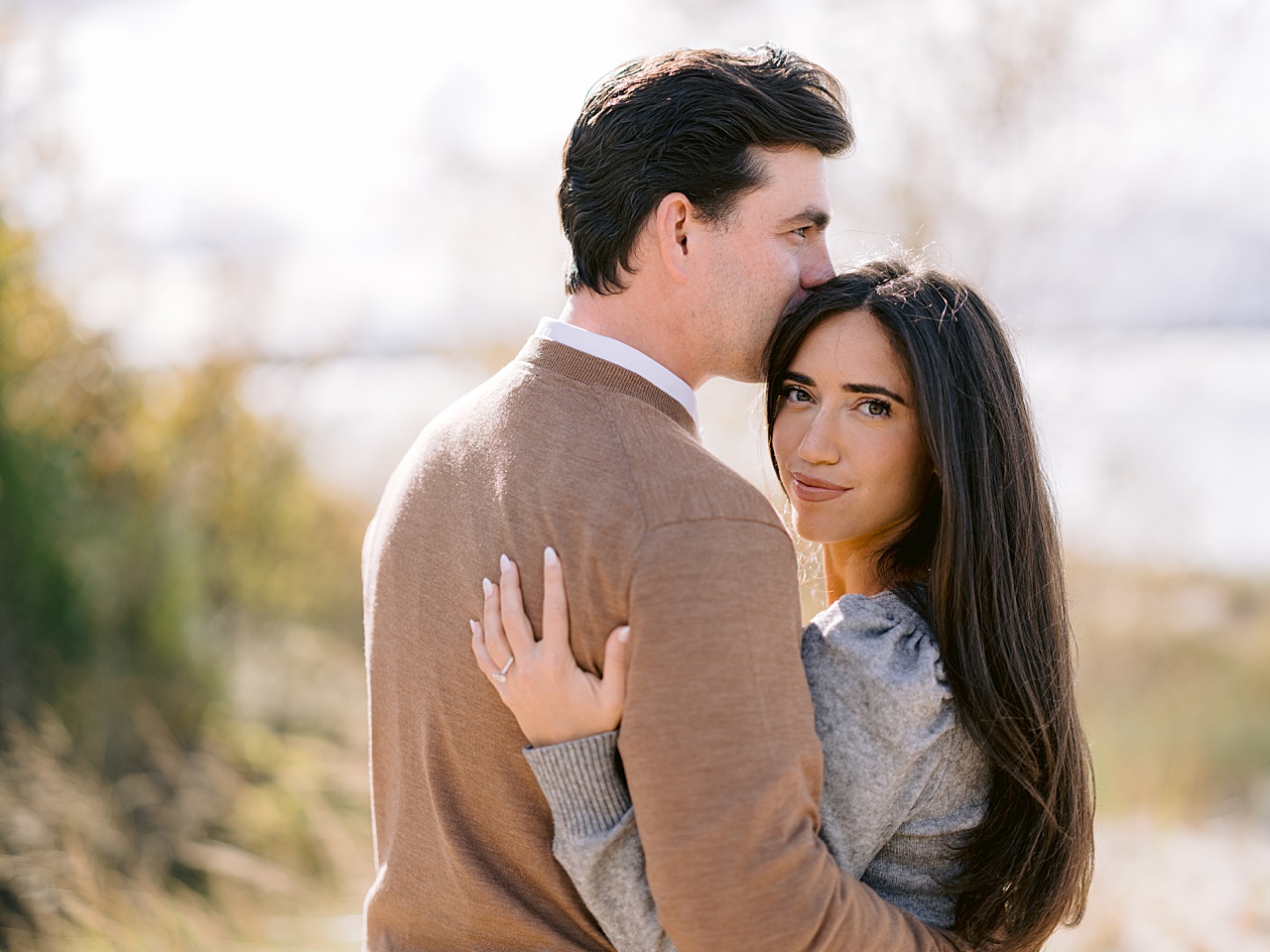 A woman wears an engagement ring and looks over her fiancé's shoulder