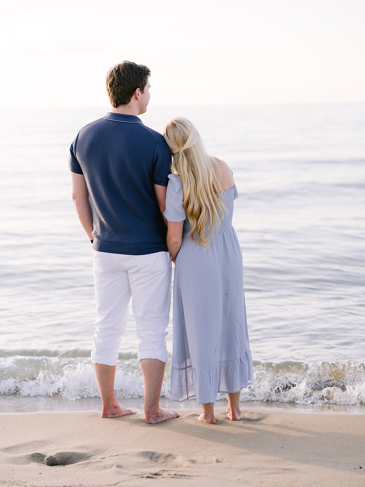 A woman resting her head on her fiancé's shoulder looking out at the sunset on Lake Michigan