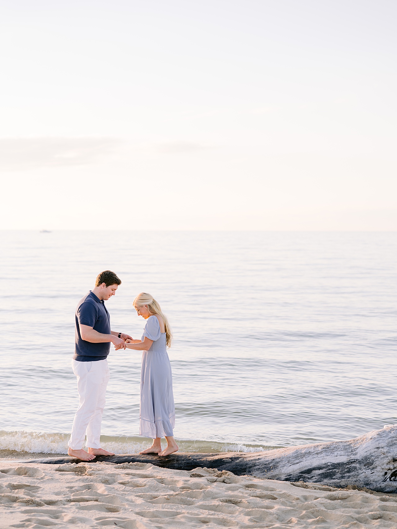 A couple holding hands and walking across driftwood