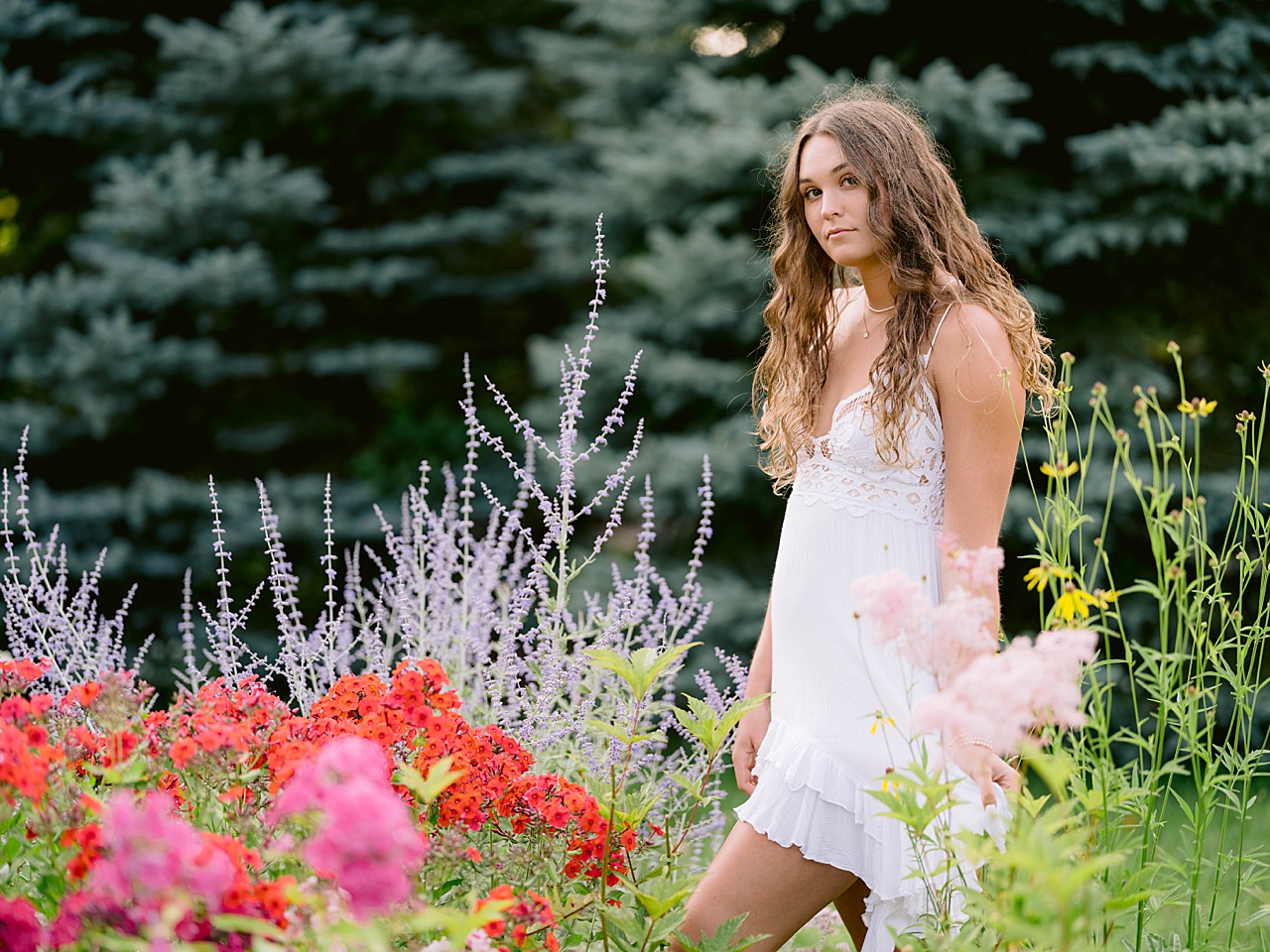 A girl in a white dress walks among flowers for senior portraits