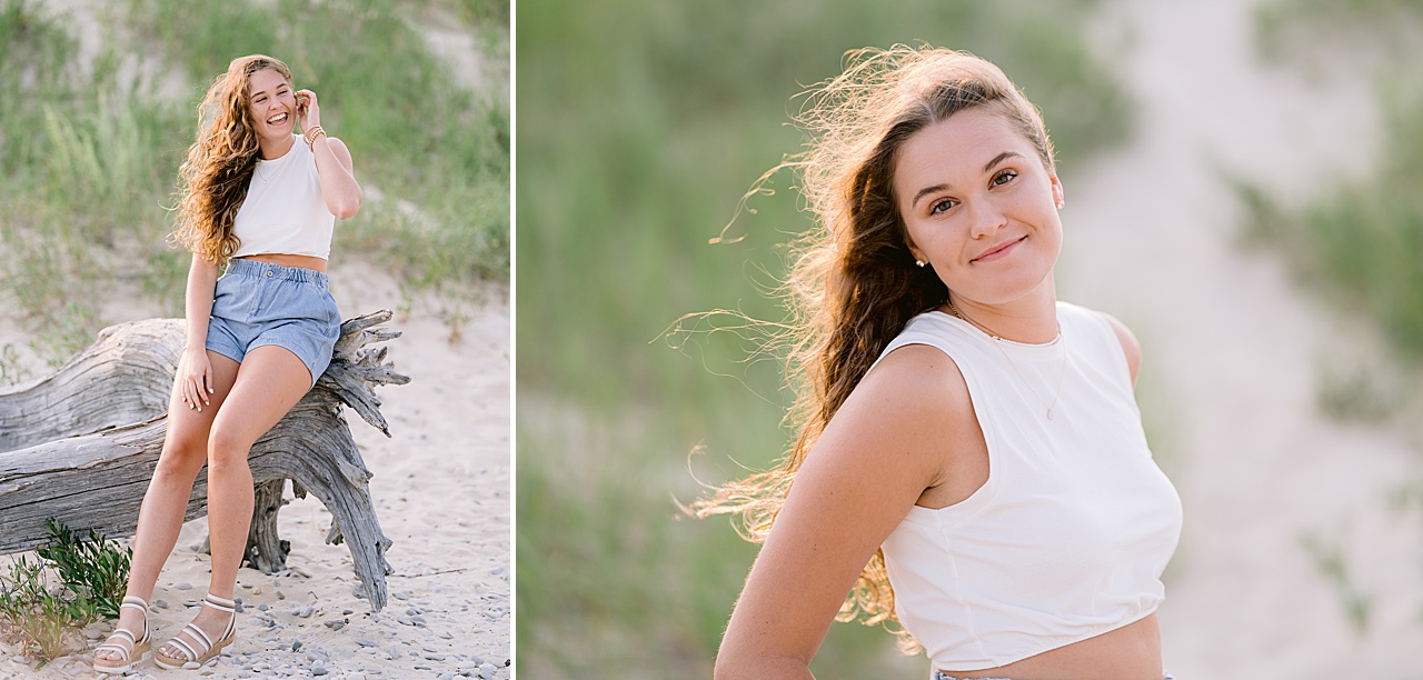 A girl sits on a very large piece of driftwood and laughs while the wind blows her hair