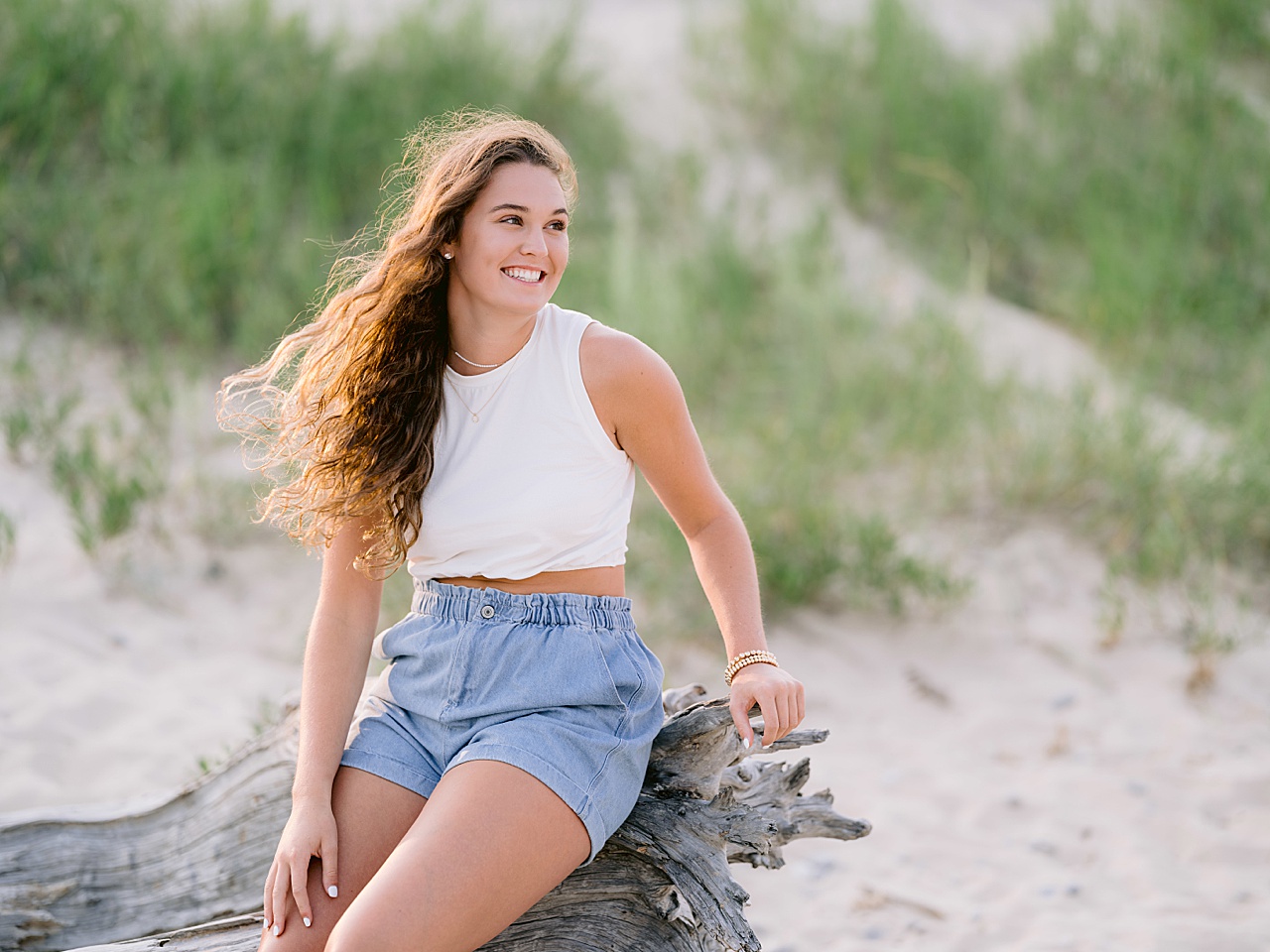 A young woman poses on a piece of driftwood for harbor springs senior portraits