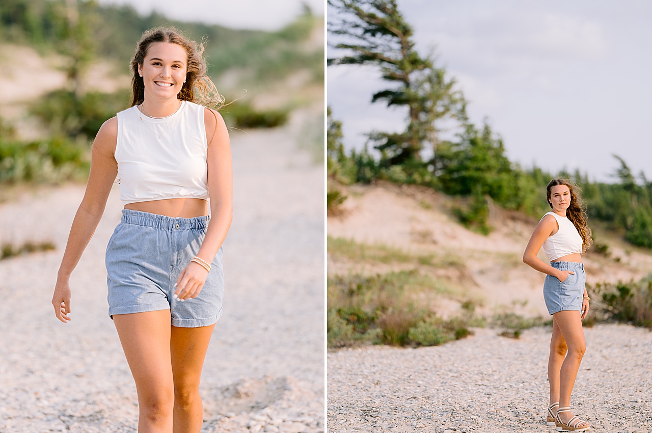 A high school senior walks up a pebbled beach and smiles for senior photos