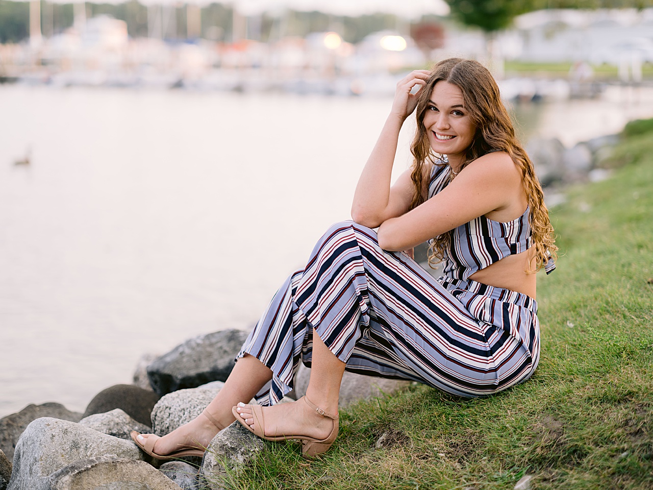 A senior girl sits beside a lake for harbor springs senior portraits