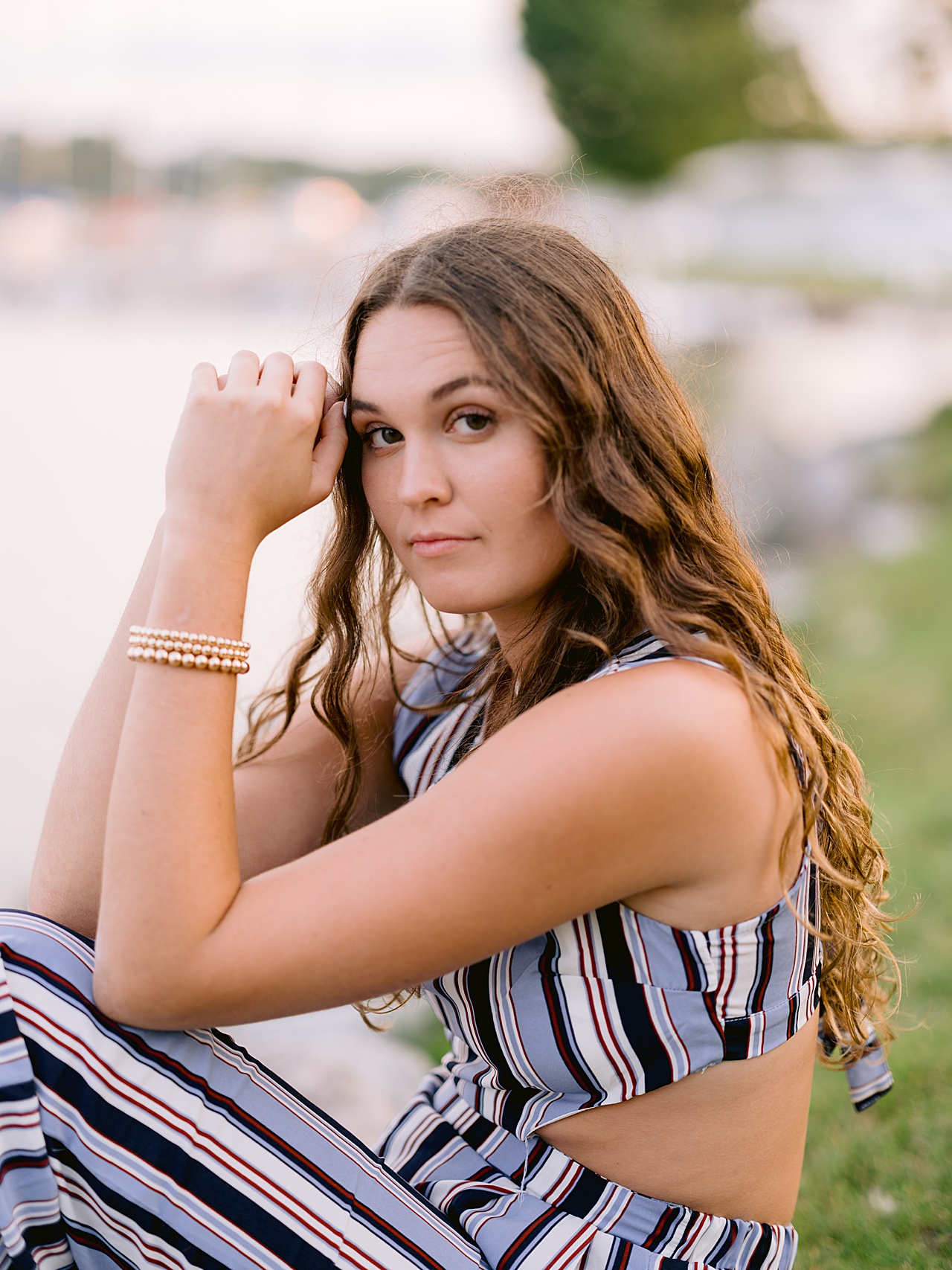 A girl leans with her head on her hands beside a lake for harbor springs senior portraits