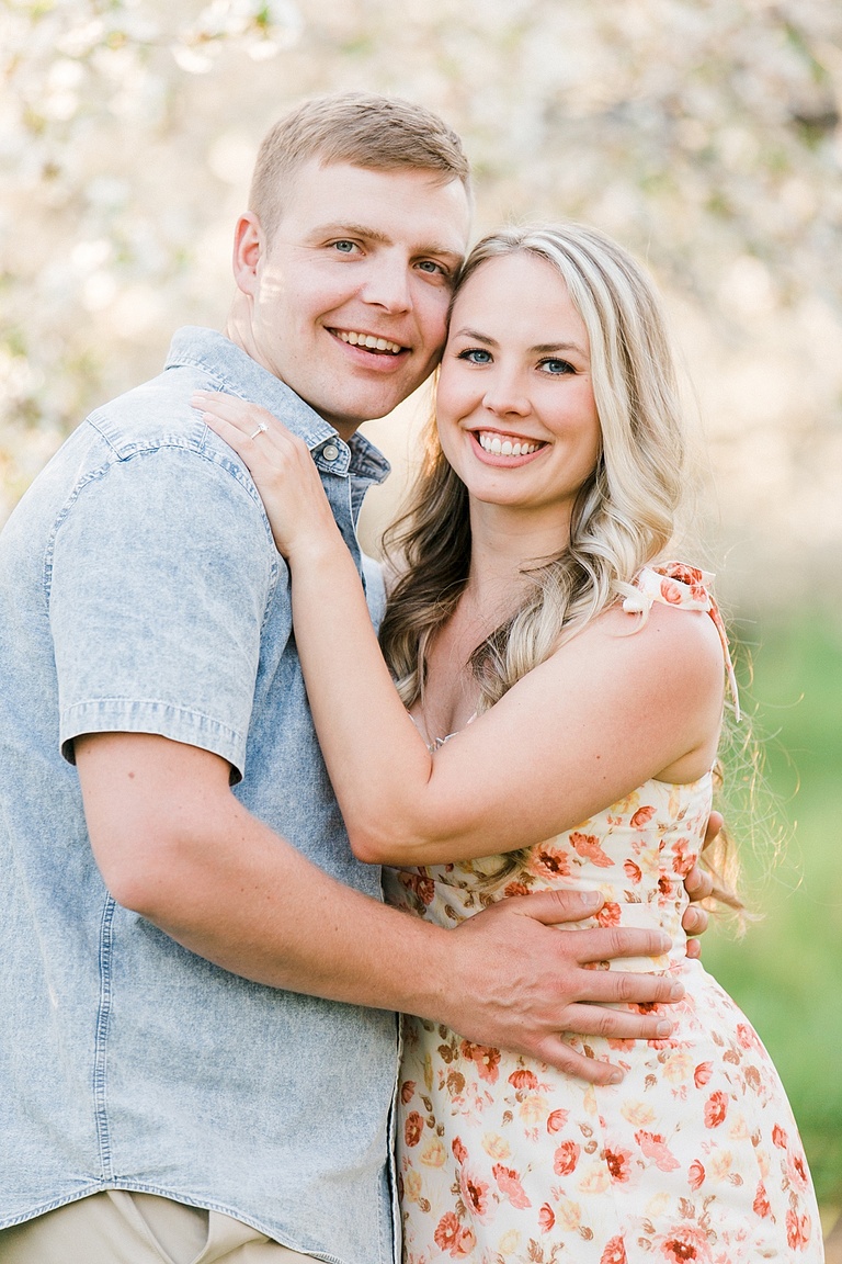 A couple smiles during an engagement session with their arms wrapped around each other