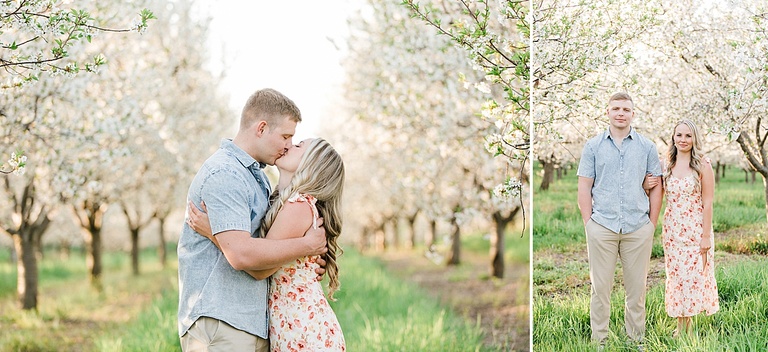 A couple poses for photographs while standing in tall grass under cherry blossoms