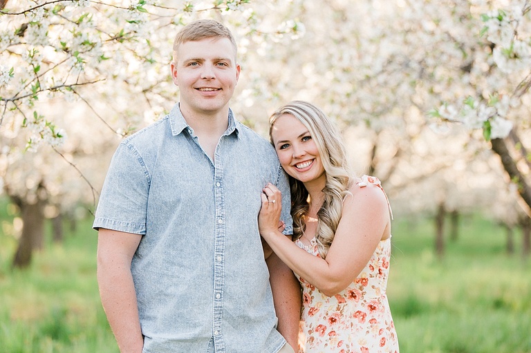 A man stands in an orchard of cherry blossoms while a woman leans her head on his shoulder