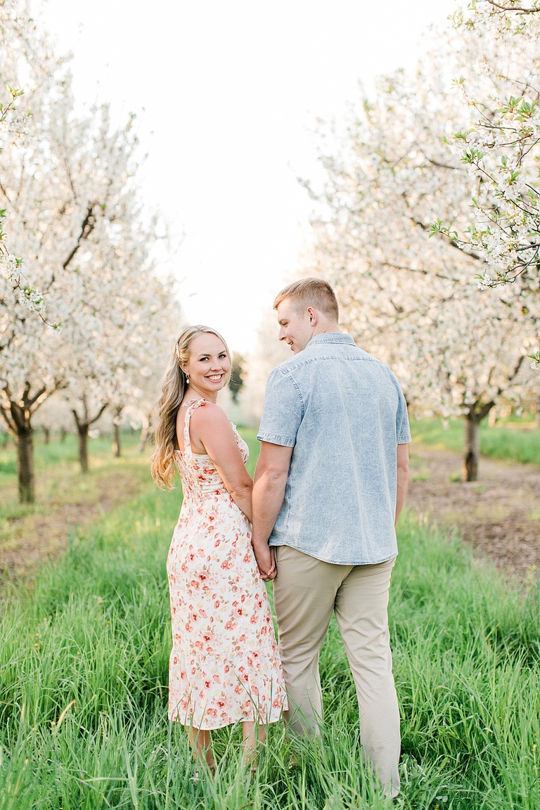 A woman in a white and pink dress looks over her shoulder and smiles while her fiancé looks at her