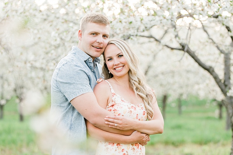 An engaged couple poses for michigan cherry blossom engagement portraits in the spring through branches