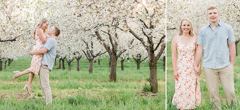 A man lifts a woman in a white dress off the ground while standing in green grass under cherry blossoms