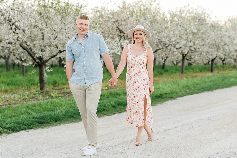 A couple holding hands walks down the gravel road of a cherry orchard in Northern Michigan