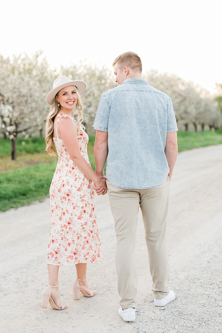 A couple walks down a gravel road for michigan cherry blossom engagement portraits