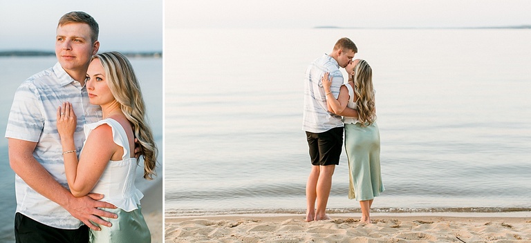 A couple kiss each other while standing on a sanding michigan beach looking out over a lake