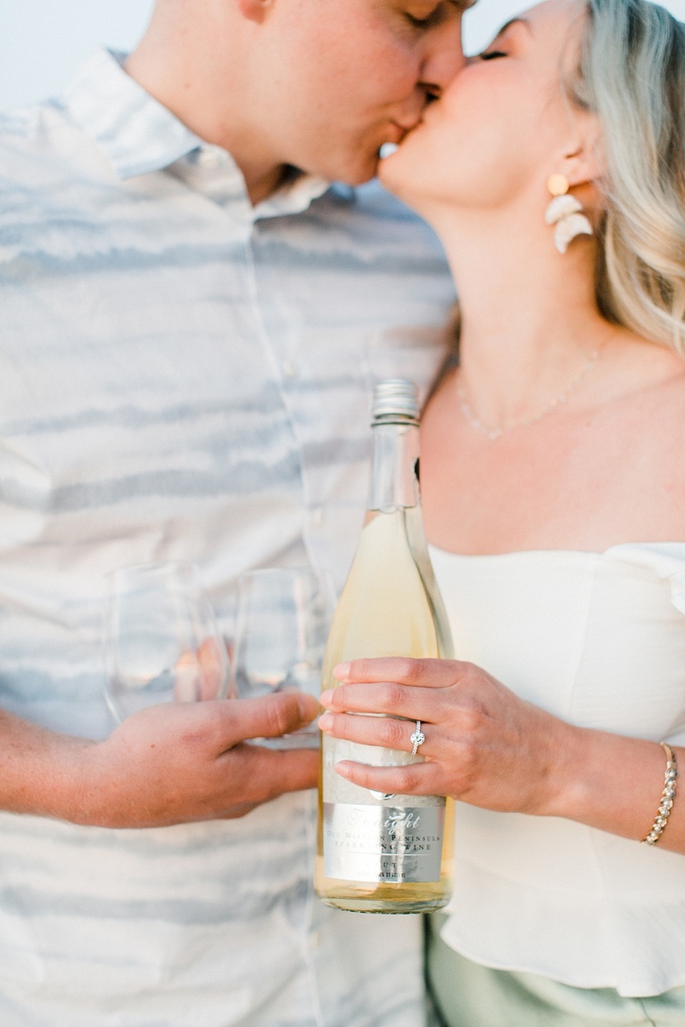 Close up of a couple holding glasses and a bottle of sparkling wine while kissing out of focus
