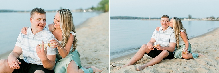 A couple look at each other and clink glasses while sitting on a beach in northern michigan