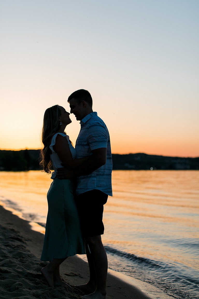 A silhouette of a couple taking engagement photos standing on a Northern Michigan beach during a sunset