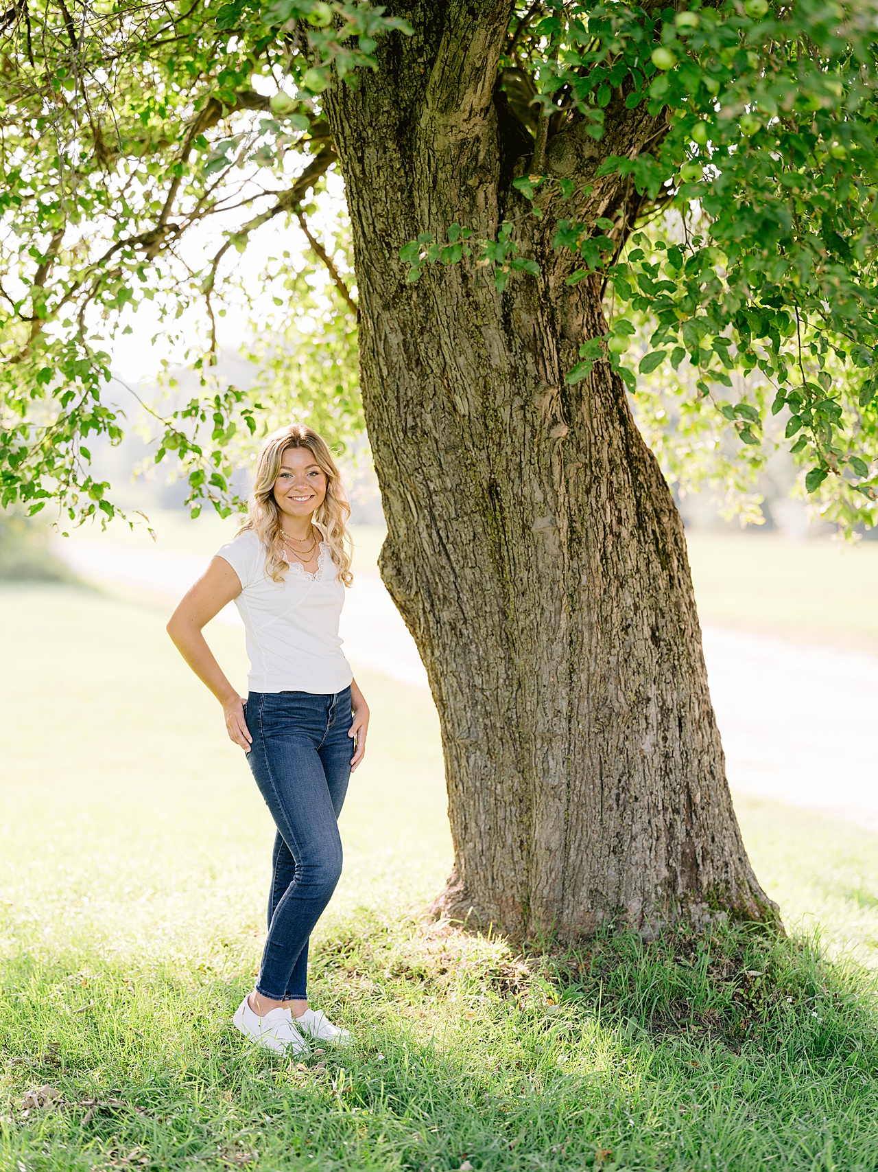 A young girl stands under a large, old tree in the countryside in northern michigan