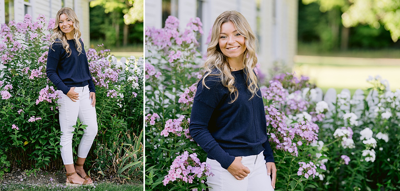 A young woman poses for michigan countryside senior portraits in front of white and purple flowers