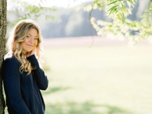 A girl leans agains a tree trunk and smiles while golden sunshine outlines her in michigan