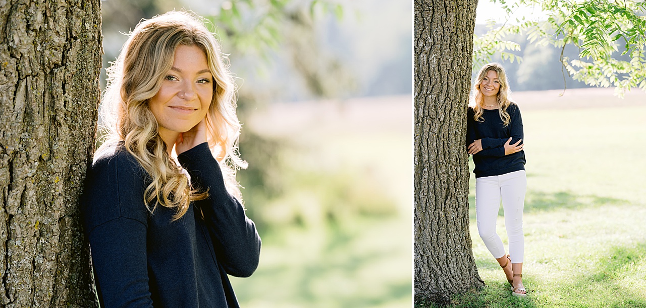 A young woman smiles and leans against a tree while posing for senior photos