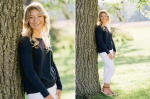 A high school senior smiles and laughs while leaning against a tree for portraits