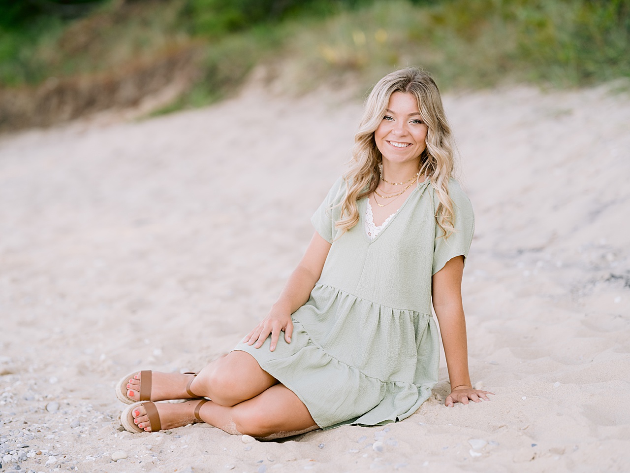 A girl sits on the beach in a green dress and smiles for michigan senior portraits