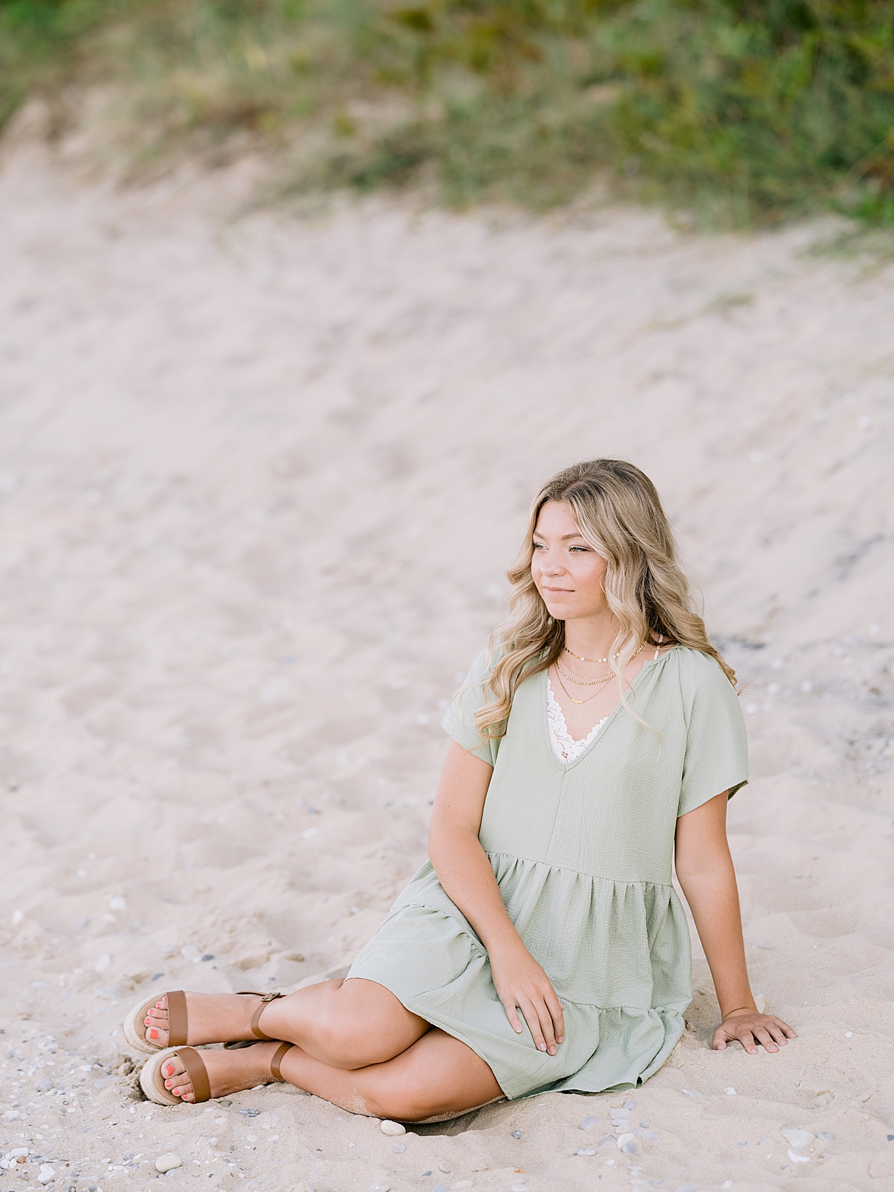 A young woman sits in the sand and looks off in the distance near Lake Michigan