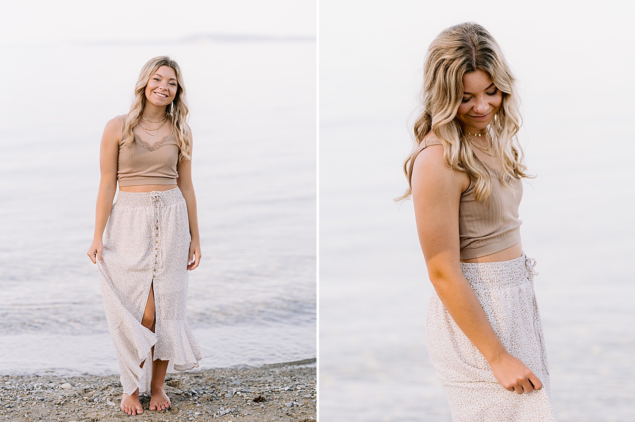 A high school girl holds her skirt and turns for senior portraits next to a lake