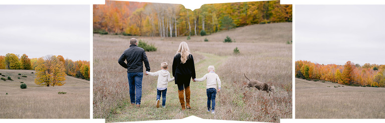 A family walks through a field in the fall while a dog leaps in tall grass