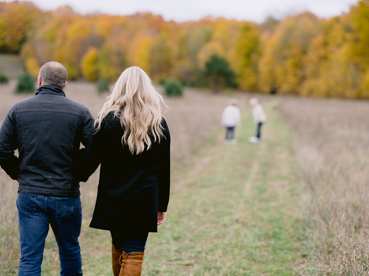 A couple walks together down a path while they're kids play in the distance