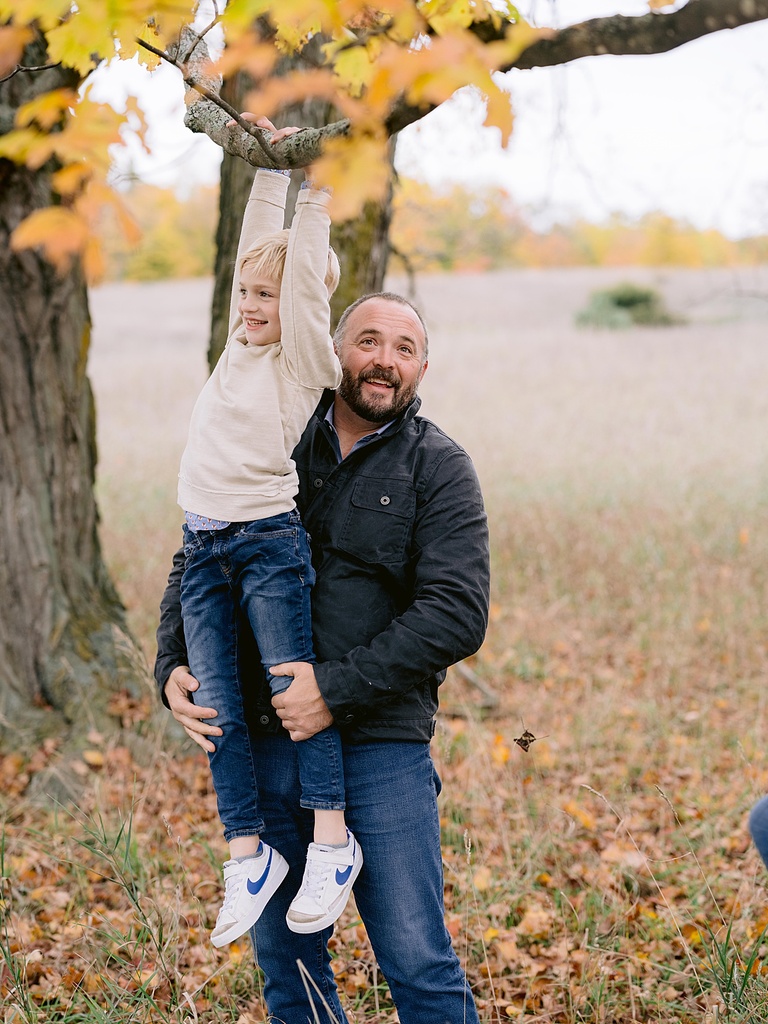 A father lifts his son up onto a tree branch for michigan fall family portraits