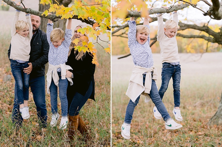 Two young boys dangle from a tree branch and smile for photos
