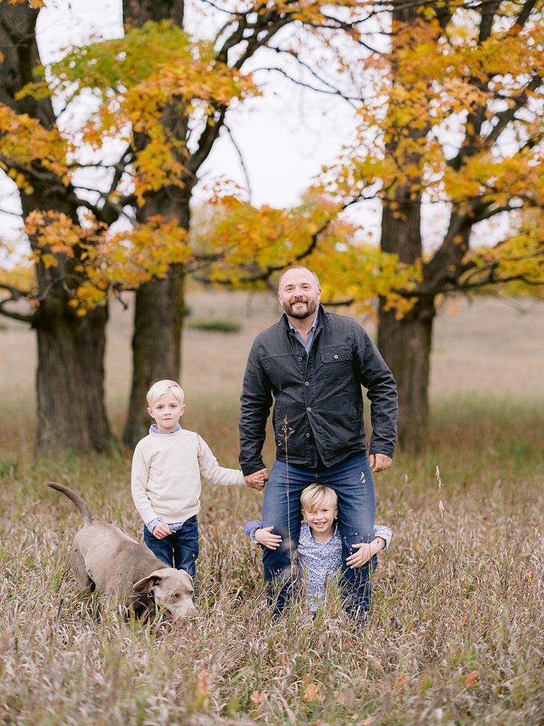 A father stands in a field with his two young sons for michigan fall family portraits