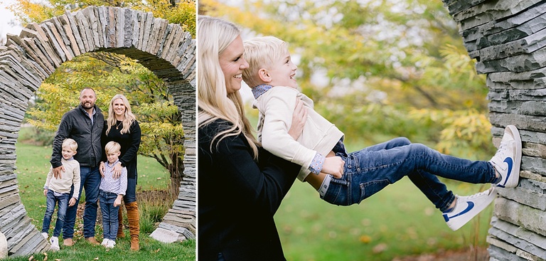 A mother lifts her son to help him climb a stone arch for michigan fall family portraits