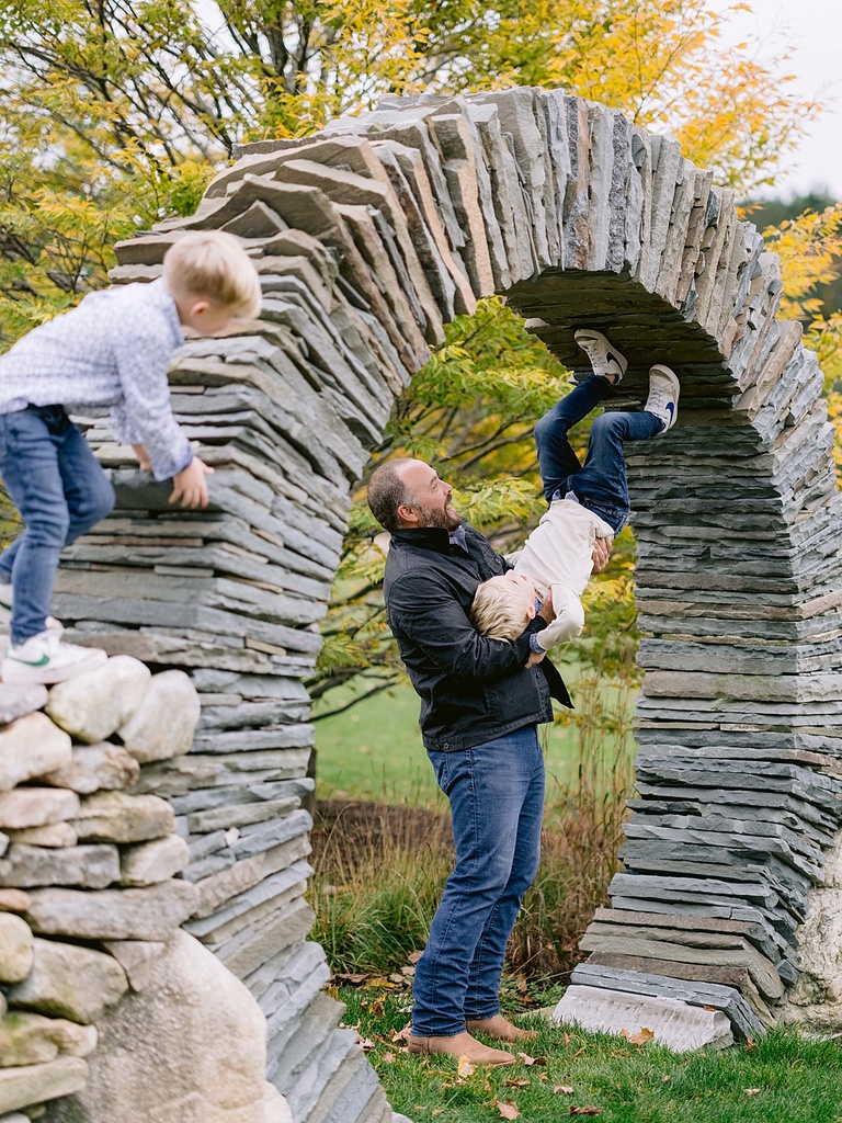 A father tips his son upside down to walk on an arch's ceiling for michigan fall family portraits