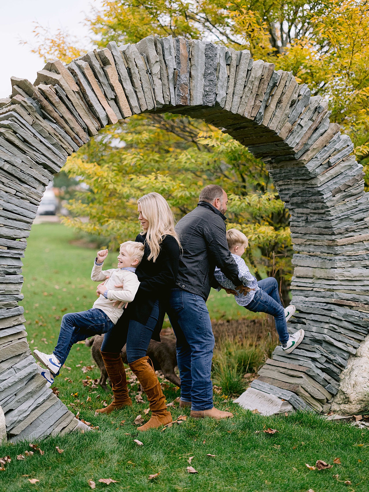 A mother and father help their two young sons play on some stones in the fall