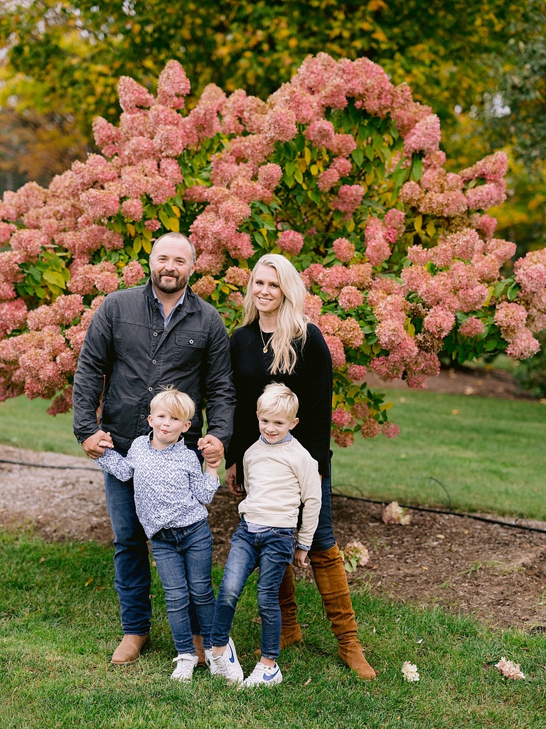 A family of four smiles and poses for michigan fall family portraits in front of pink hydrangeas