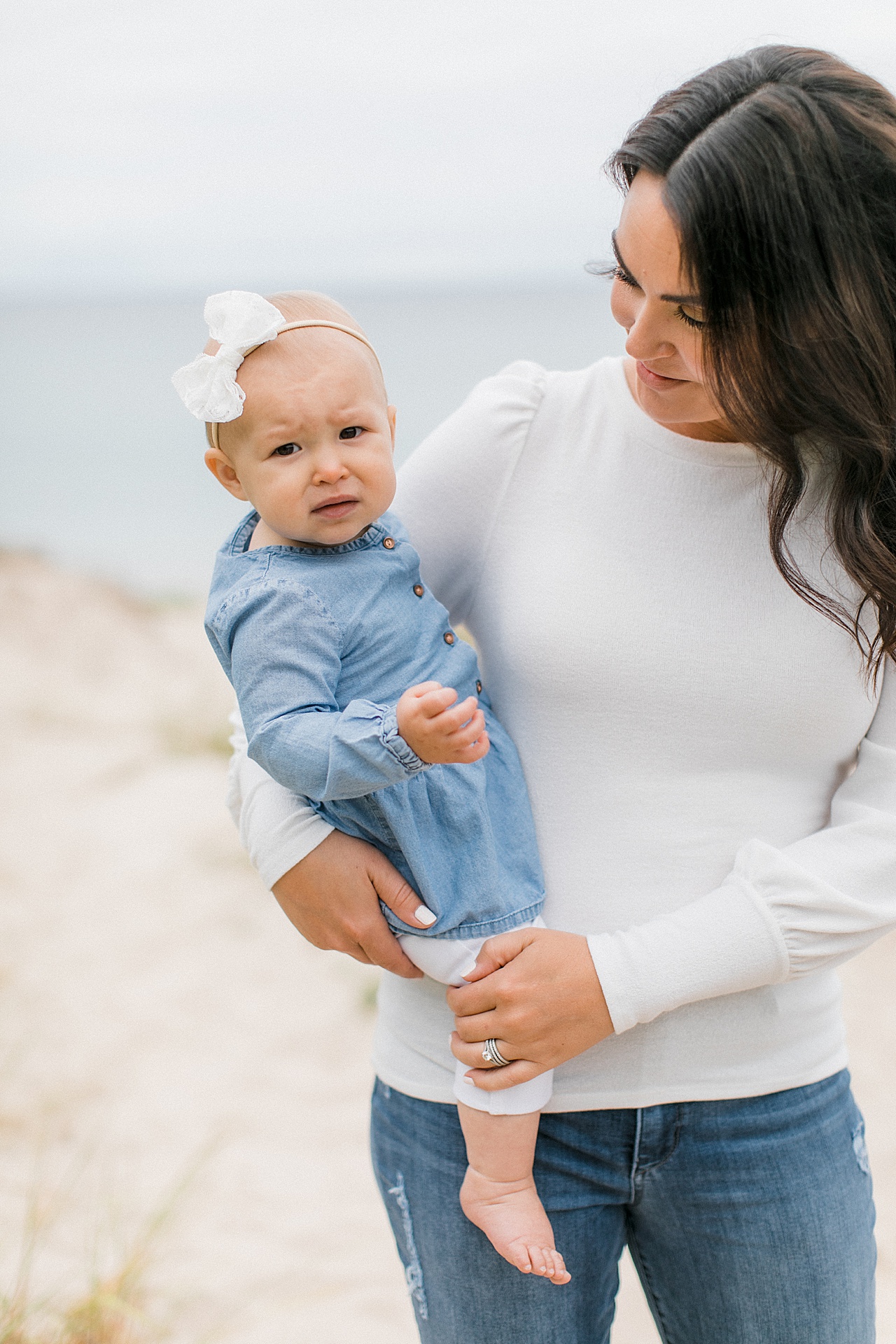 A photograph of a mother holding her baby girl on her hip on a beach in Michigan