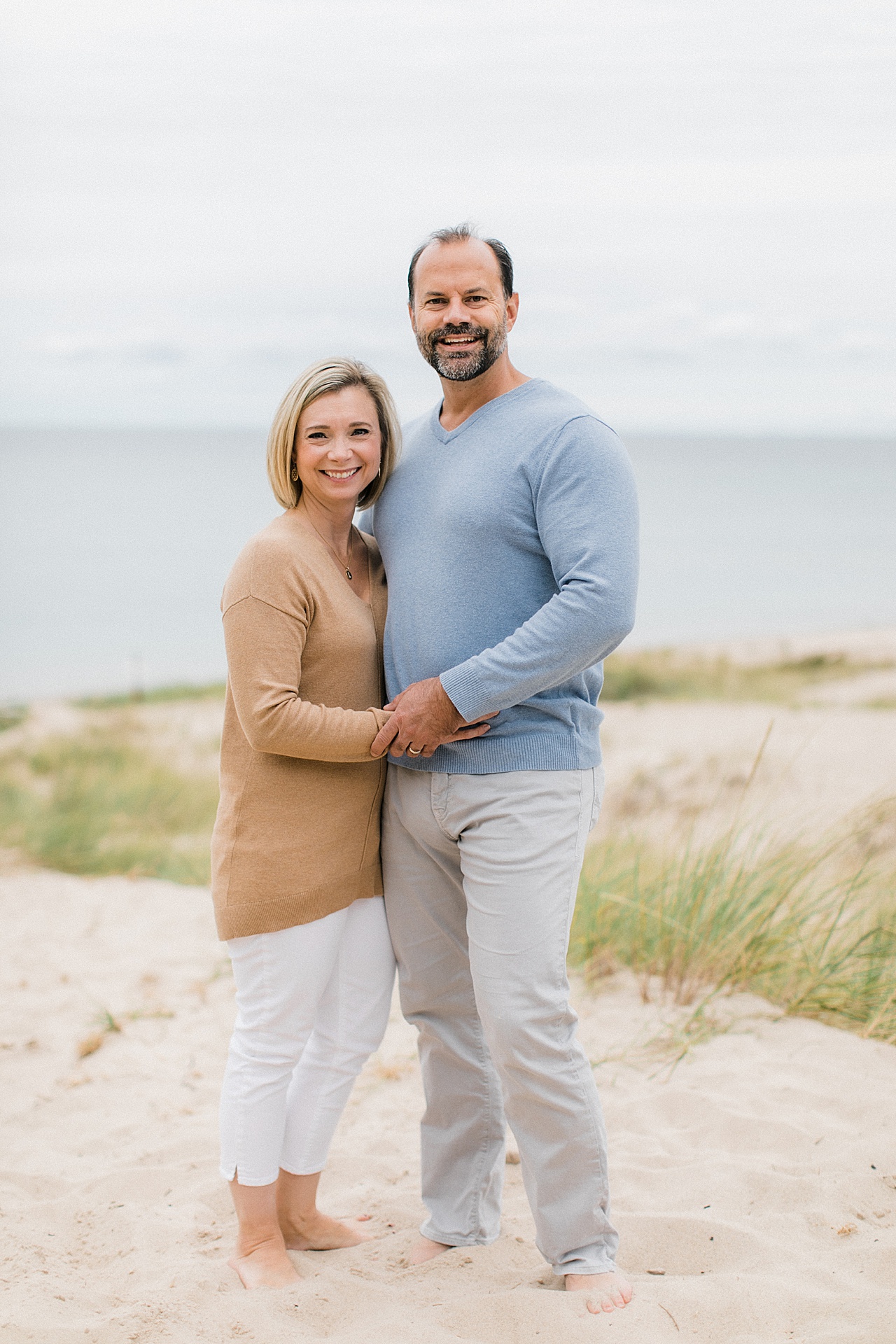A couple stand holding hands and smiling for beach photos in Northern Michigan
