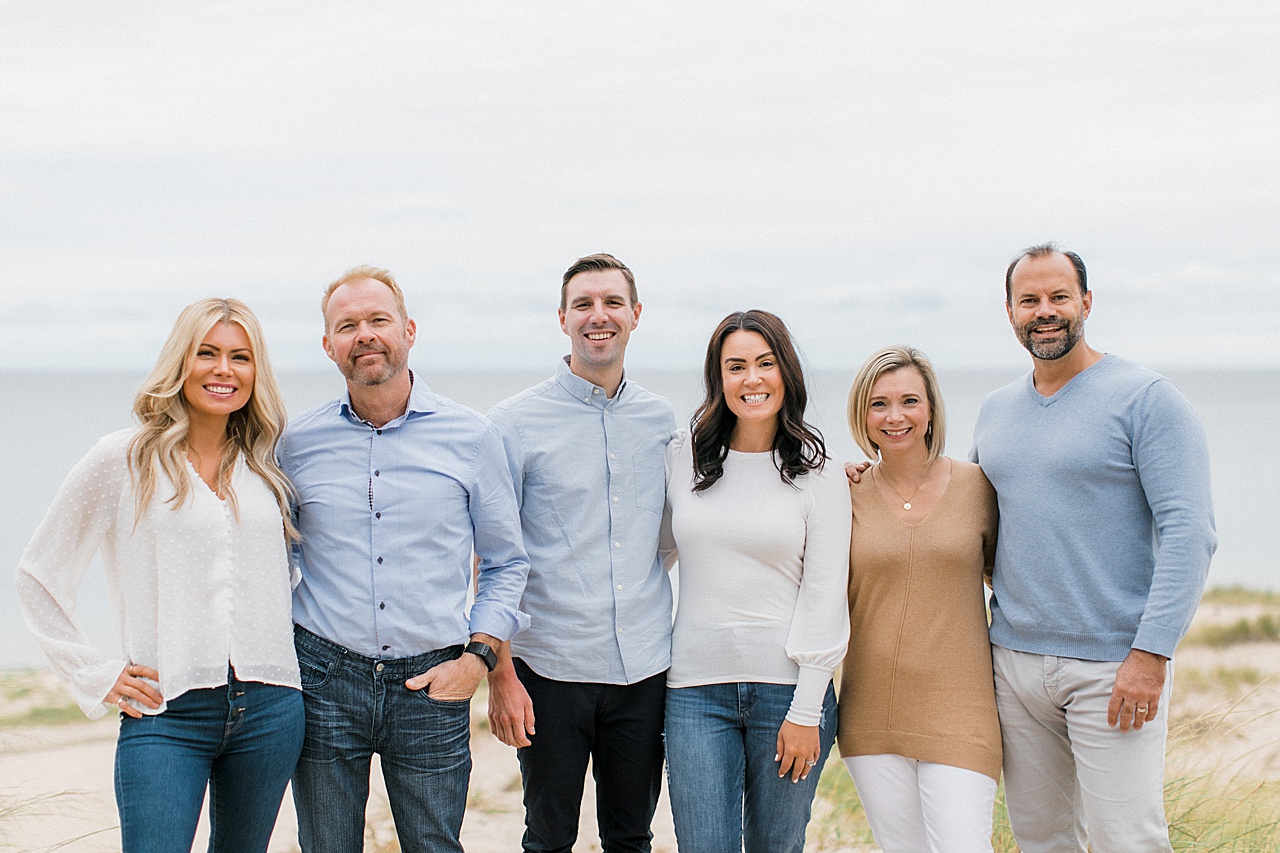 A family wearing shades of white, tan and blue pose together on a grassy beach