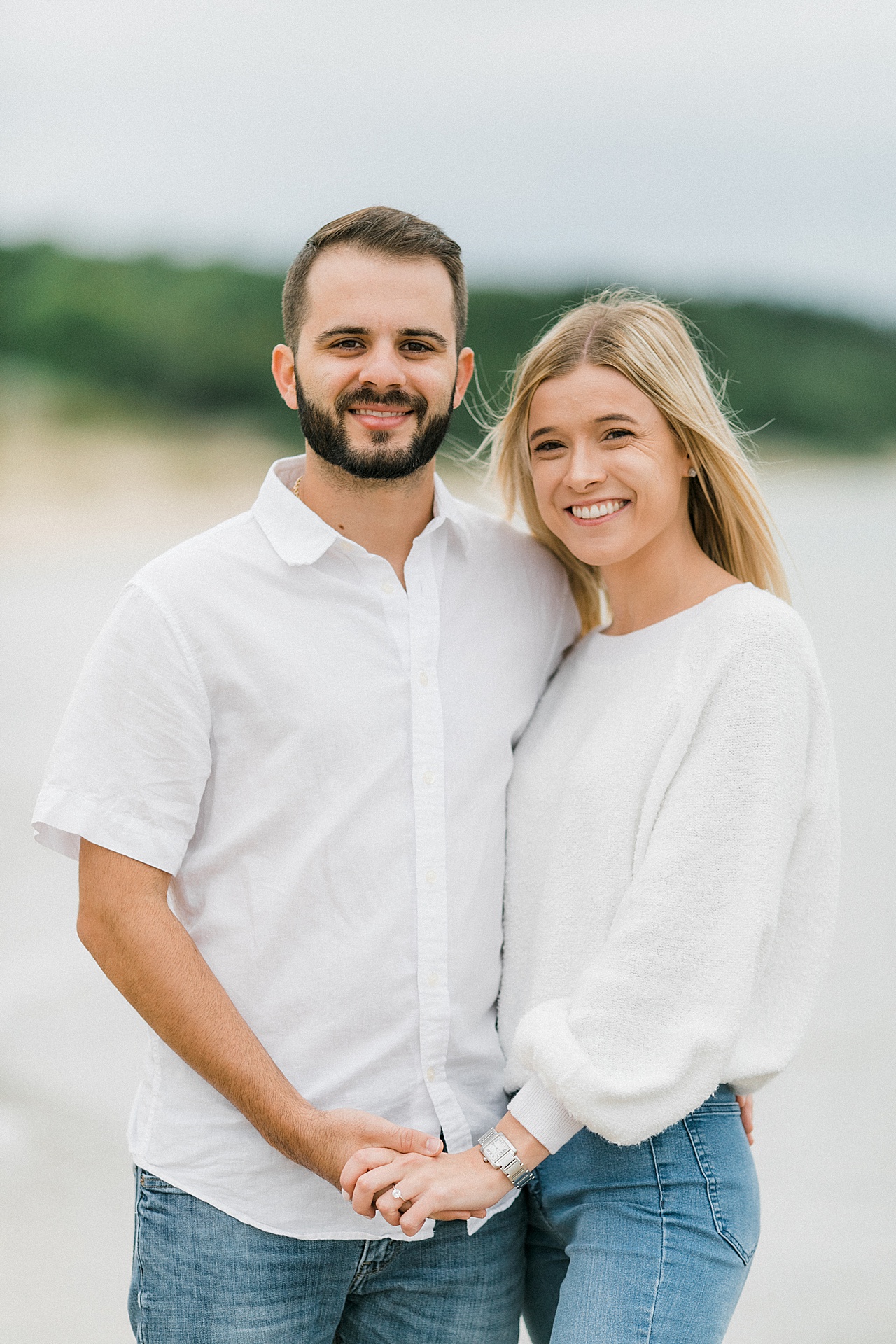 A couple holds hands and smiles while dressed in white shirts and blue jeans