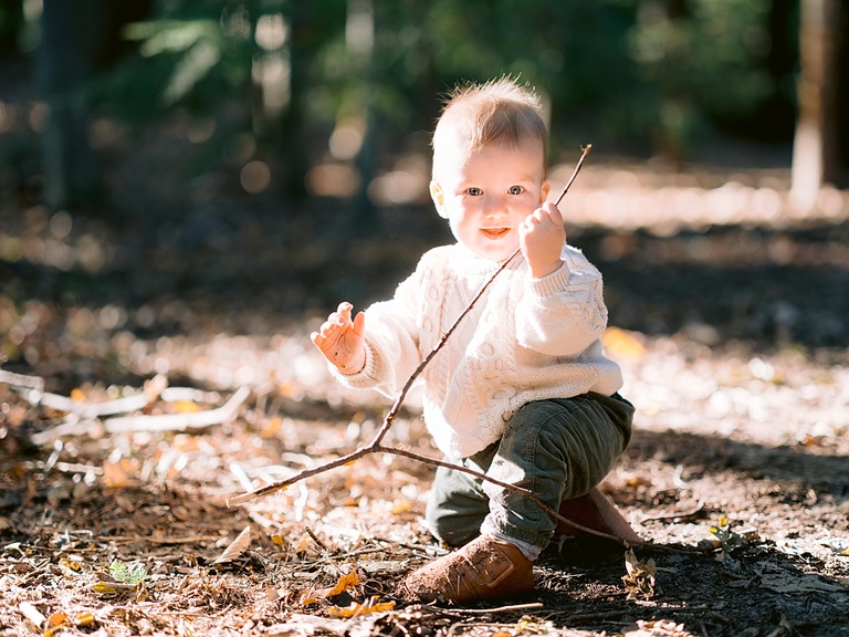 A one year old boy playing with sticks in the woods